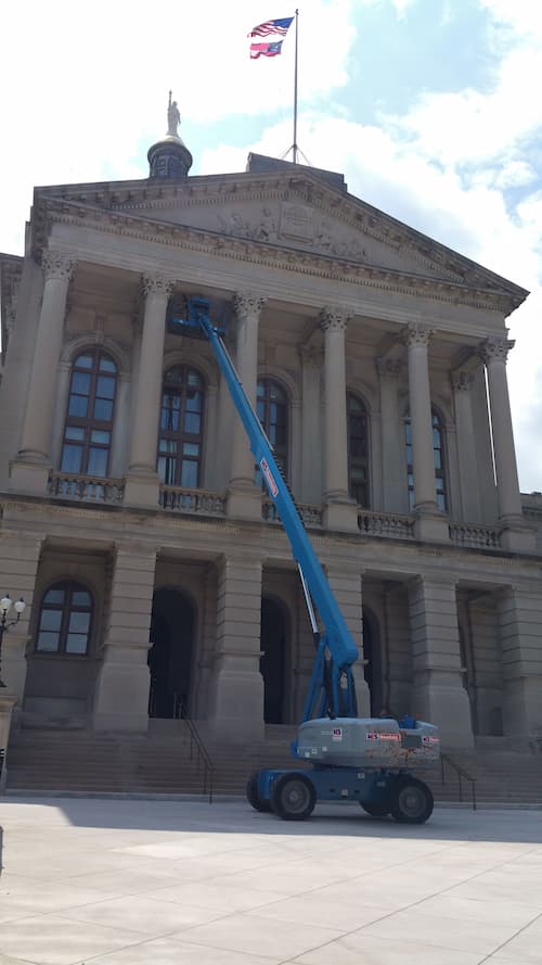 A cherry picker extended to the upper columns of a governmental building.